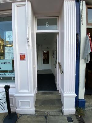 White wooden door with glass panelling. Turn silver metal handle and push from left to open. Brown wooden handrail on right.