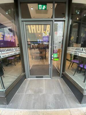 From sidewalk facing venue. Grey framed glass door ahead. Pull silver handle on right to open.