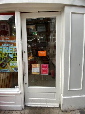 From sidewalk facing venue. White framed glass door ahead. Silver handle on left. Push to open.