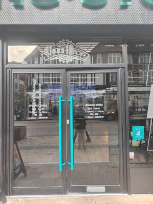 From sidewalk facing venue. Black framed double glass doors ahead. Push blue handle in centre to open.