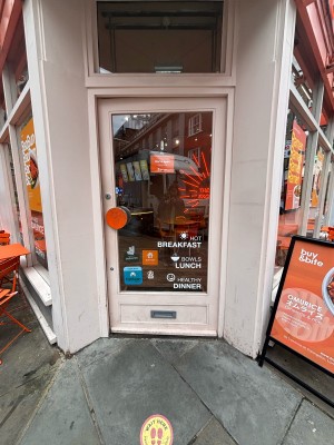 Glassed paneled door with white frame ahead. Push orange metal handle at left to open.