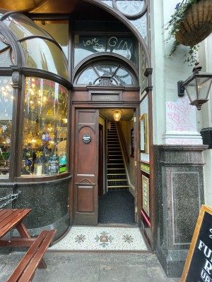 From right of picnic tables facing straight. MainFrom right of picnic tables facing straight. Main entrance ahead. Wooden door. Push on left to open.