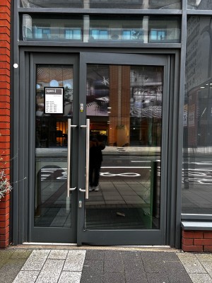 Glass door with grey metal frame. Pull handle in center to open.