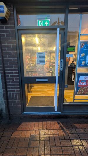 Glass door with grey frame. Push handle on right to open