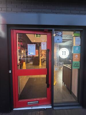 Glass door with a red frame and black handle on right. Push to open.