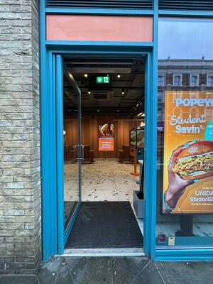 From sidewalk facing entrance. Blue framed glass doors ahead. Push handle on right to open inwards.