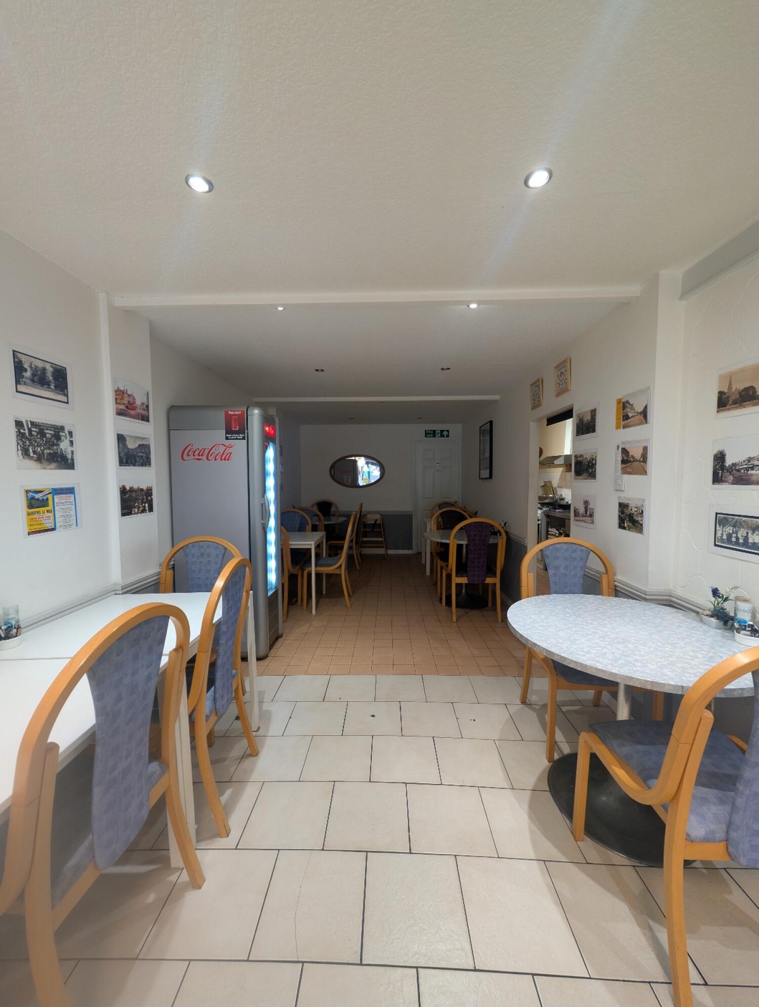 From end of counter facing straight. Tables and chairs along both sides and back. Bathroom door at back right.