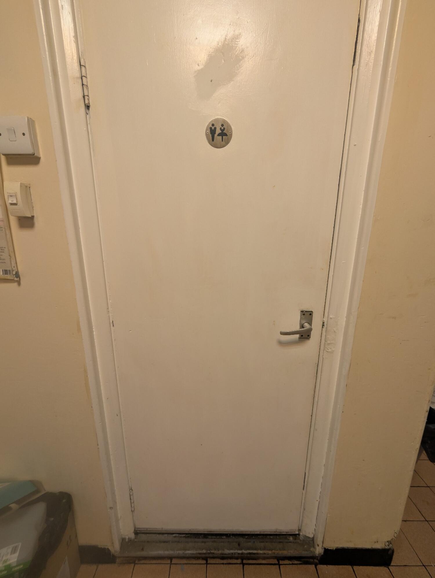 From preceding door facing right. White wooden door in front. Silver handle on right. Pull to open.