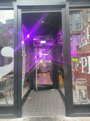From sidewalk facing venue. Black framed archway ahead. Venue door at back.