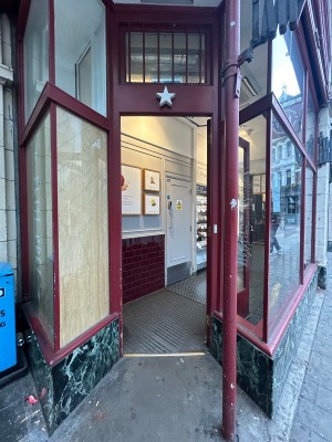 Single glass door with red frame. Push from left to open. Red pillar on right.