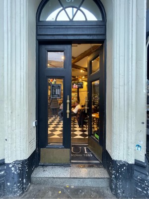 Double glass door with black frame. Push from centre to open. Doorbell for assistance to left of door.