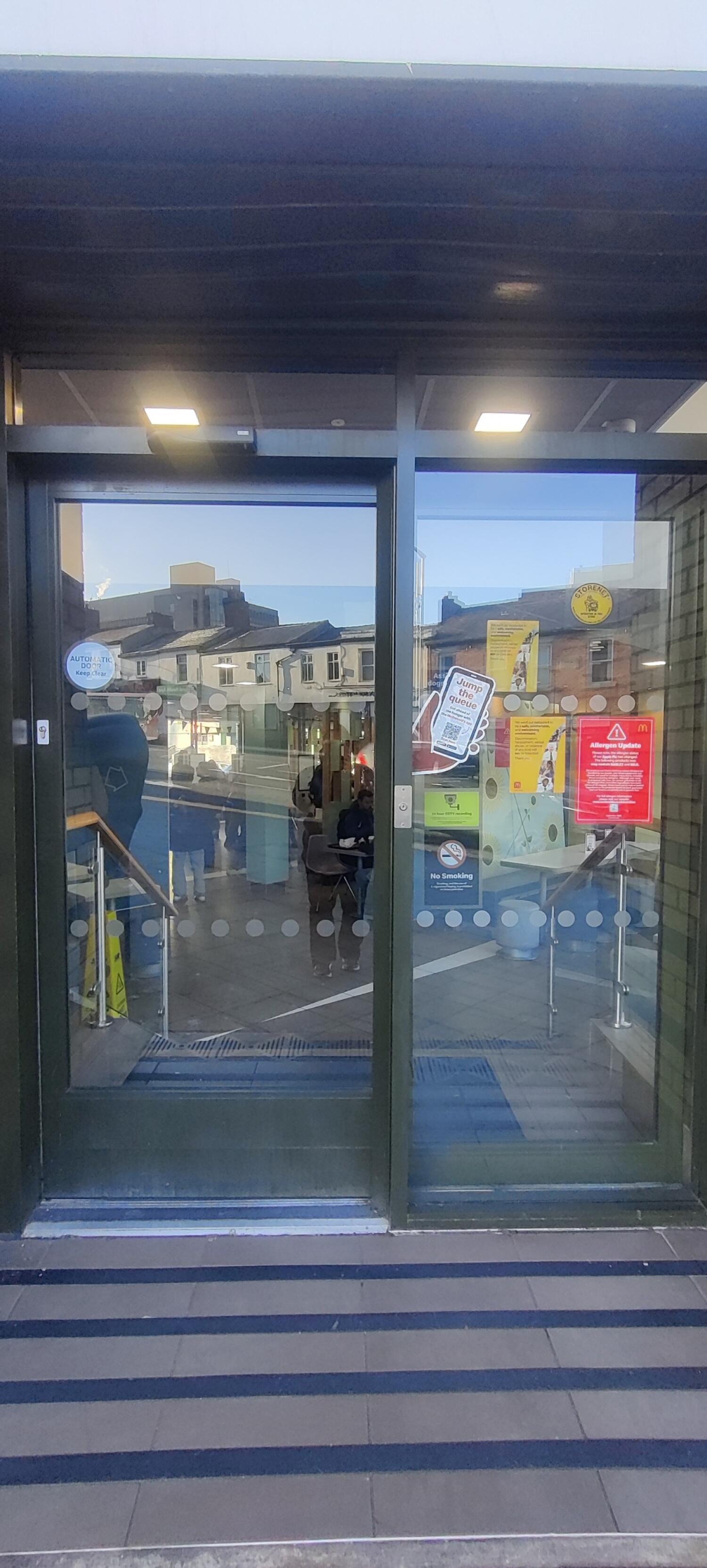 From opening, facing straight. Black metal-framed double glass door ahead.