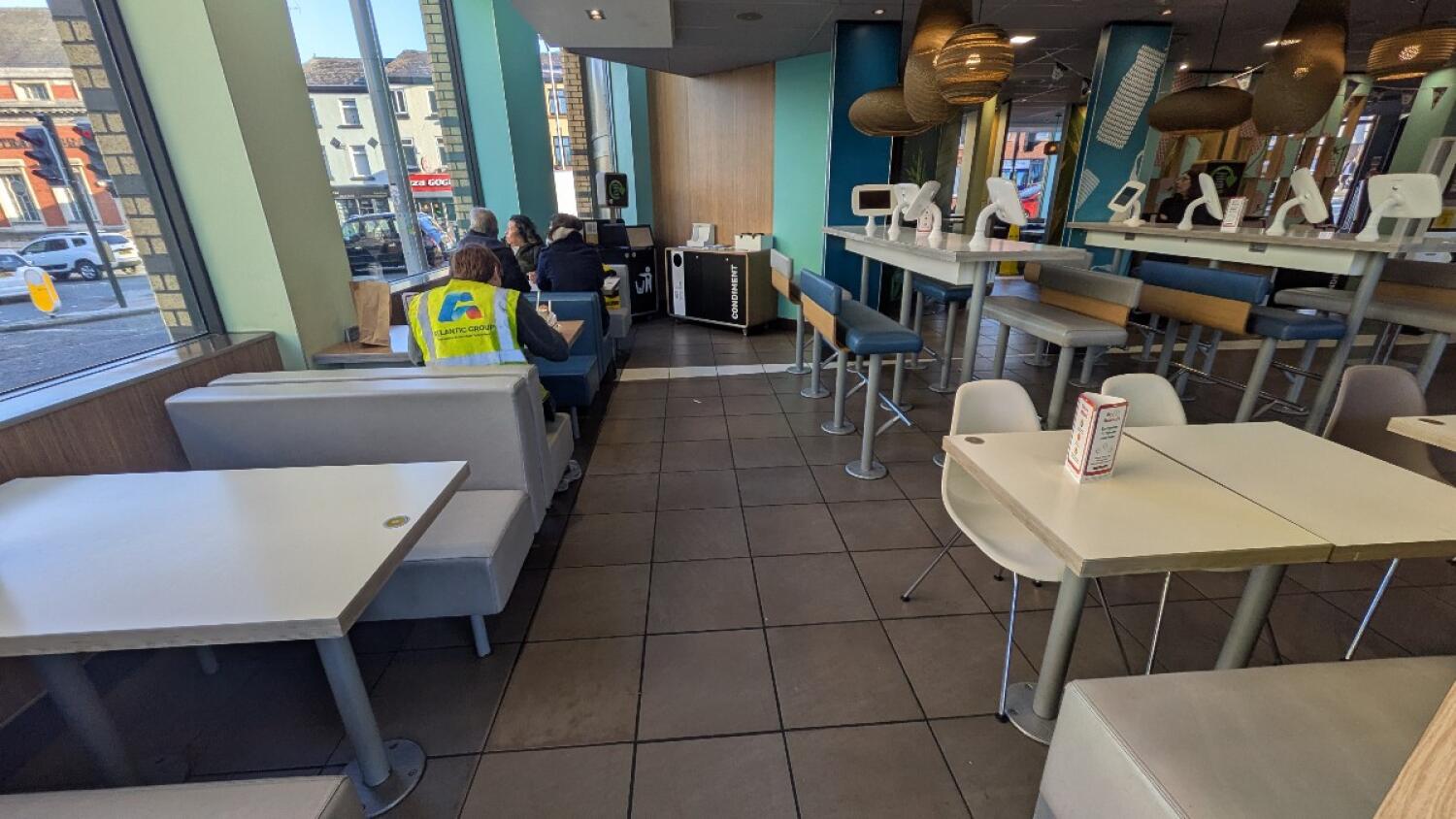 From left of divider facing straight. Booth seating along left. Path in centre. Tables and chairs right. High tables with stools along back right.