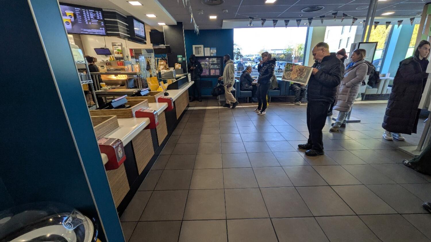 From pathway facing straight. Counter with tills along left. Path in centre. Booths along back wall right.