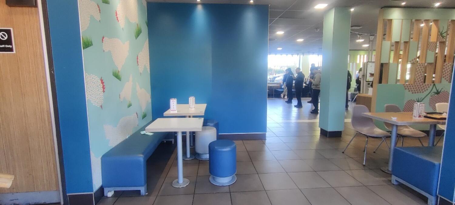 From entrance facing left. Half booth, tables and stools along left. Half-booths and chairs on right. Pillar at back right.
