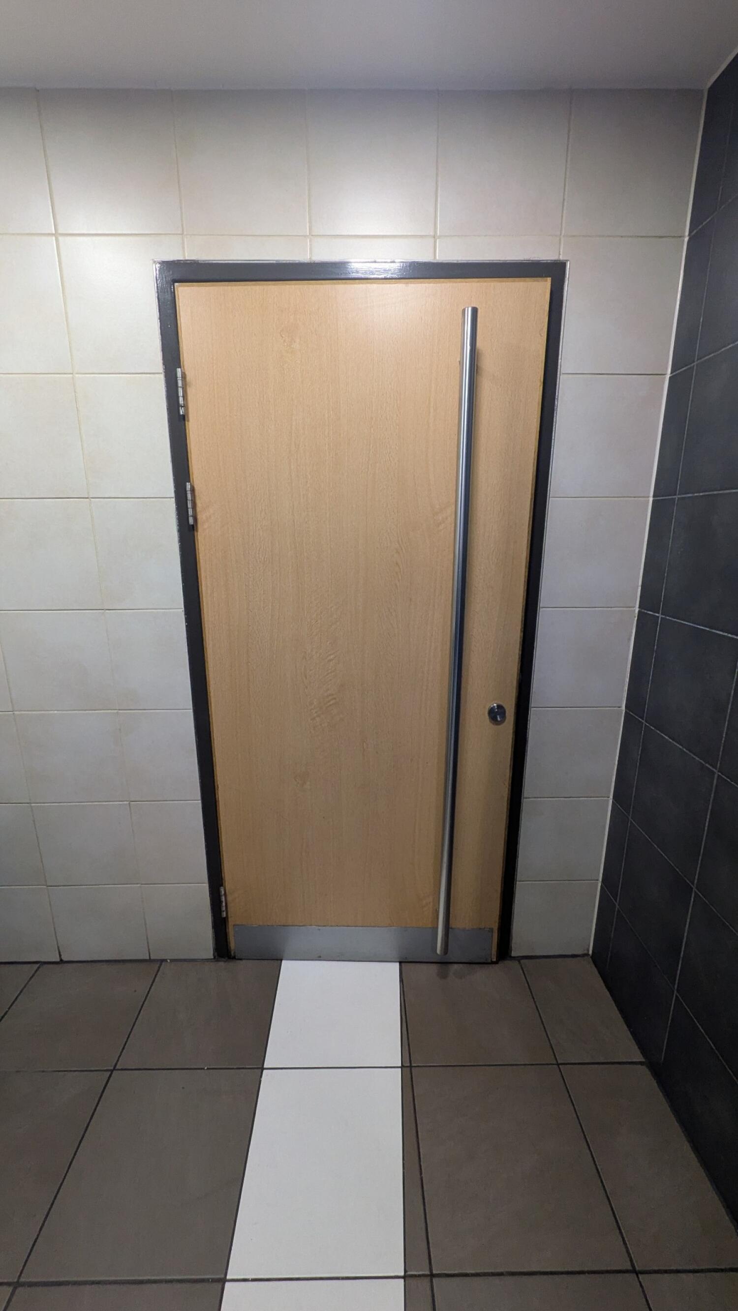 From first door facing straight. Second light wood door with metal frame. Pull from vertical handle on right to open.