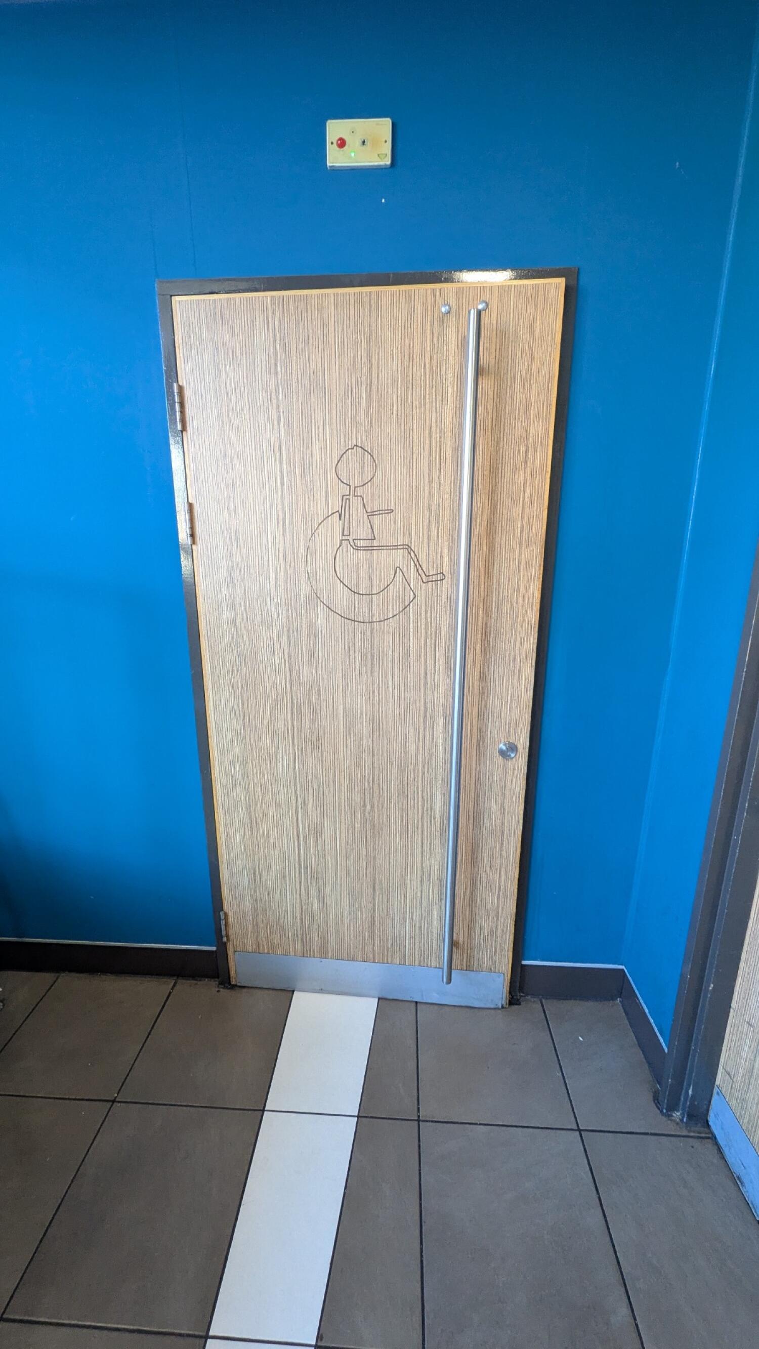 From path facing left. First light wood door with wheelchair symbol. Pull from vertical handle on right to open.