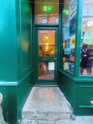 Glass panelled green door to venue with one step up. Push handle on right to open.