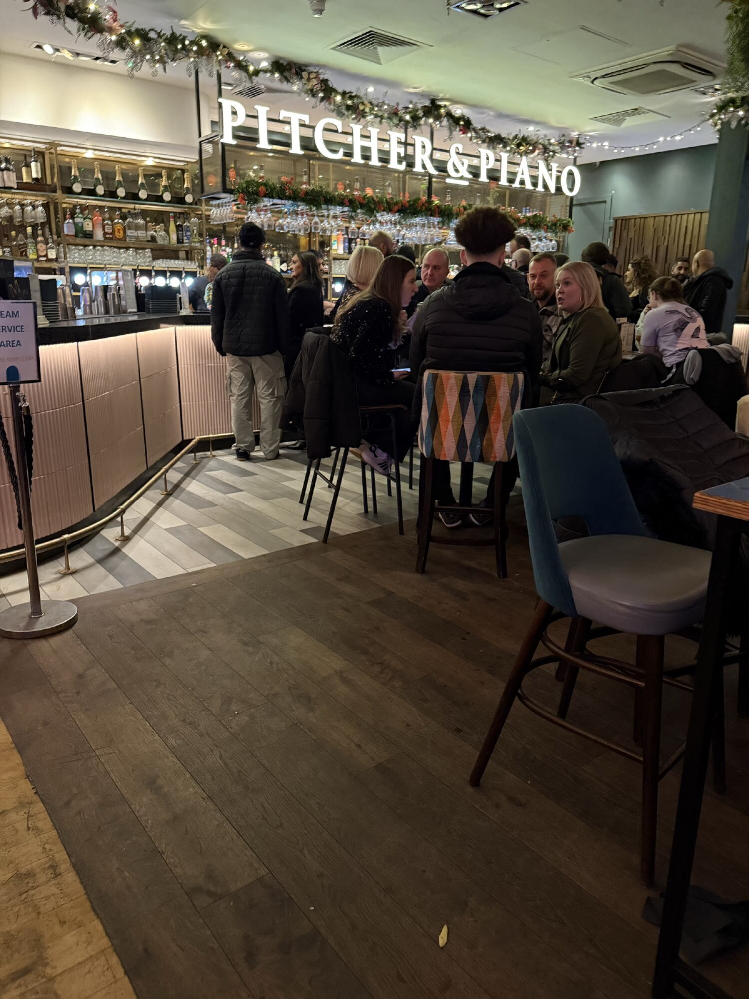 Bar counter along left with seating in front. Path in centre leading to bar. Chairs and tables along right.