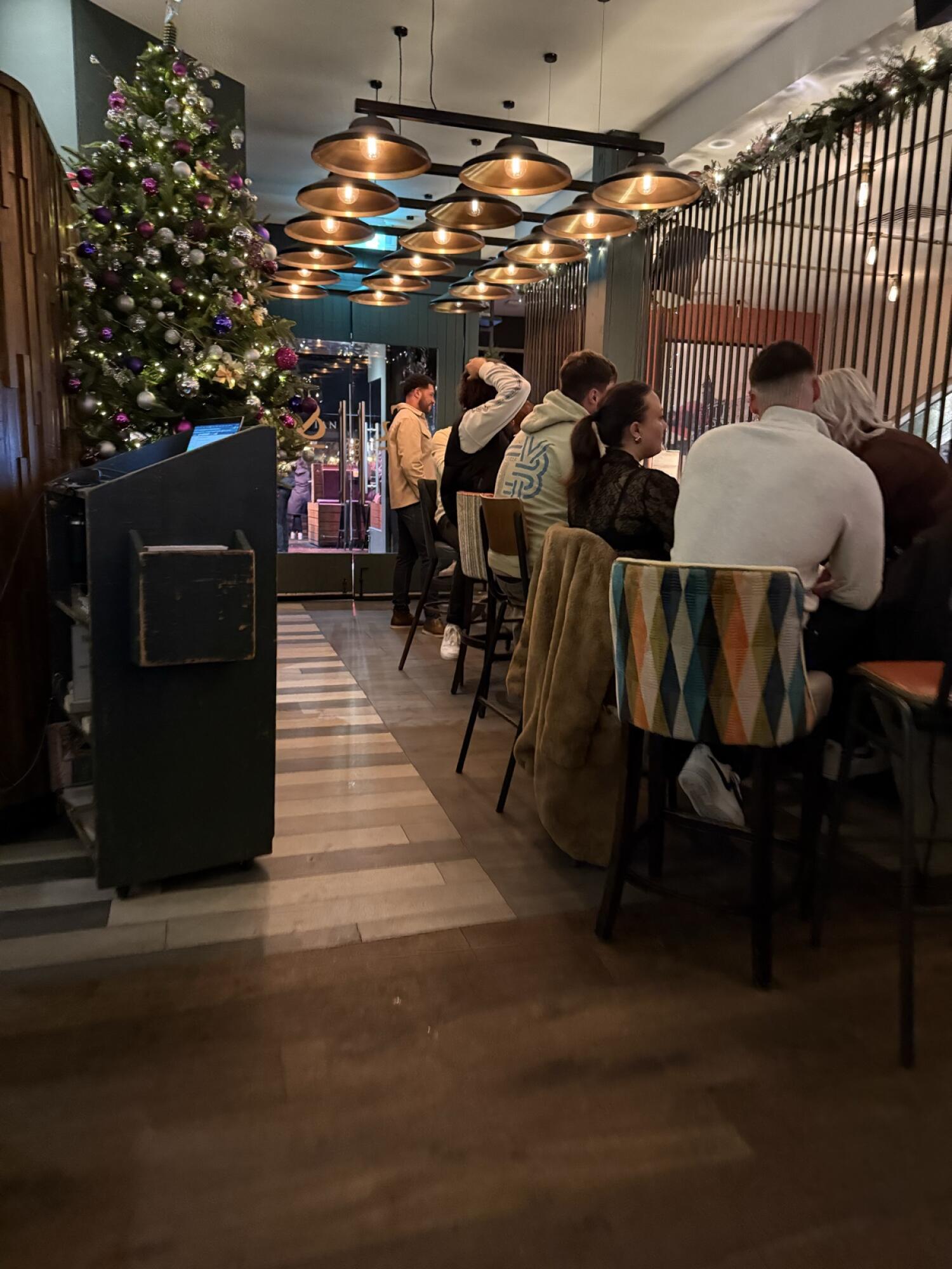 Christmas tree along left. Path in centre leading to entrance. High tables with chairs along right.