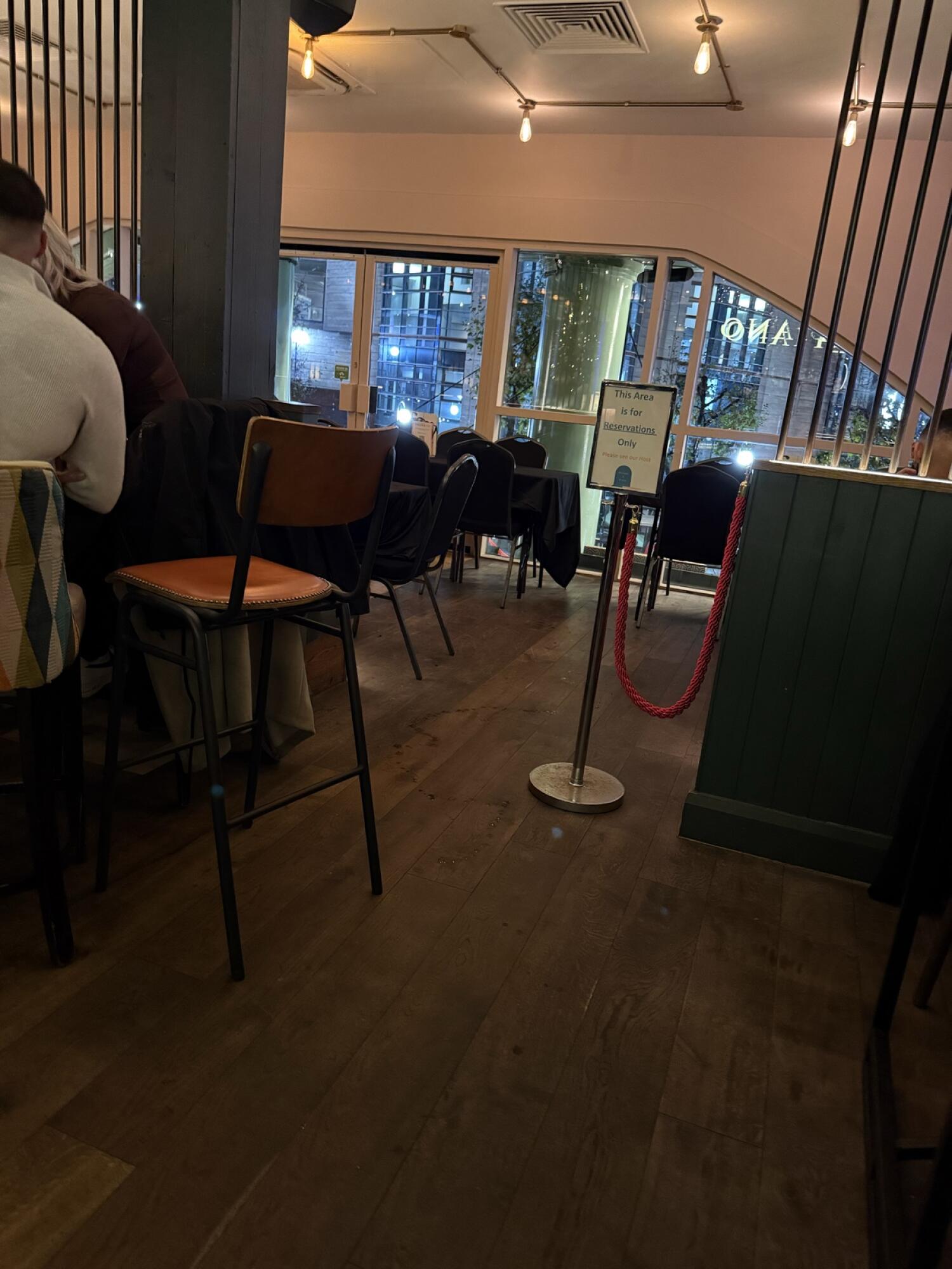 Tables and chairs along left. Path in centre with queue cord. More tables and chairs to right and back.