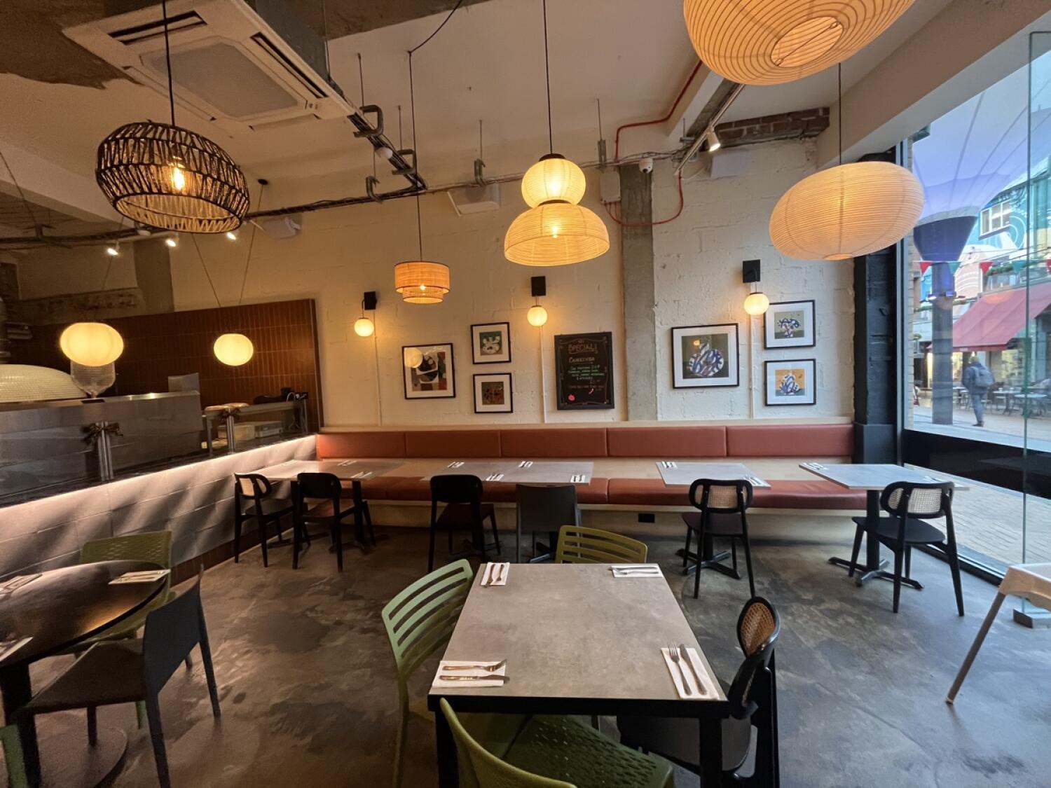From entrance facing right. Half booth along back wall. Tables and chairs in centre. Round table with chairs front left.