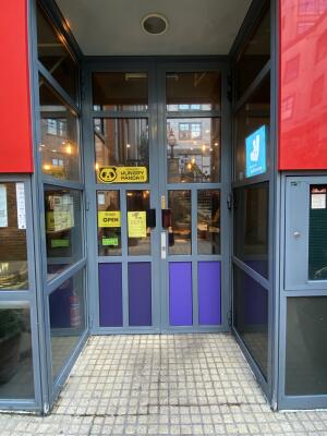 Grey framed glass door. Pull red and black metal handle from centre to open.