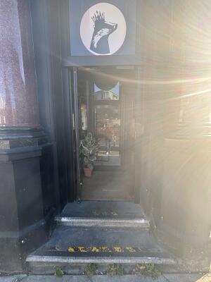 Archway ahead to entrance. Black framed glass door at back. Push door from right to open.