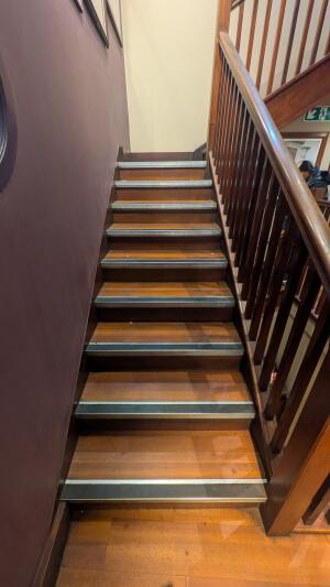 From right of side area facing right. Staircase ahead, leading up. Handrail along right side.