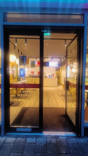 Black framed glass door to venue. Push handle in centre to open.