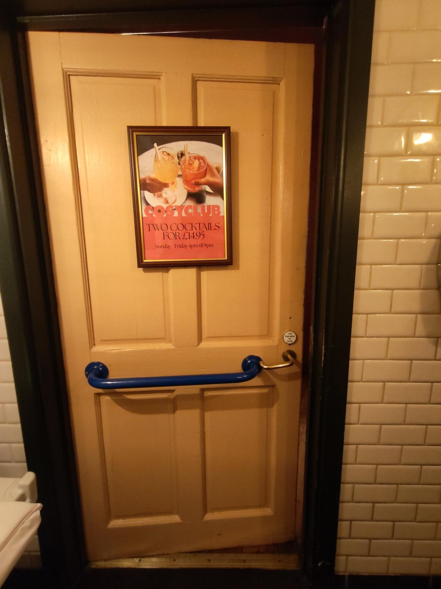 Back of door. Blue grab rail in centre. Push silver handle on right to open.