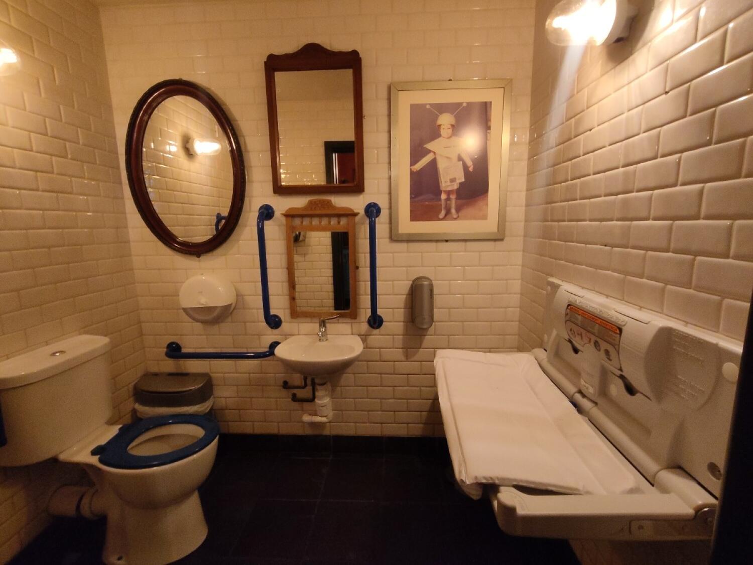 From doorway facing straight. Baby changing station on the right. Sink at back centre. Toilet on left.