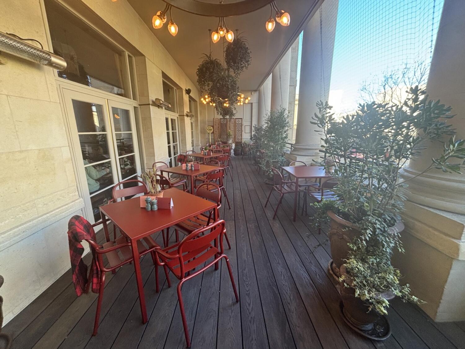 From door facing left. Tables and chairs along left and right. Planters in between along right.