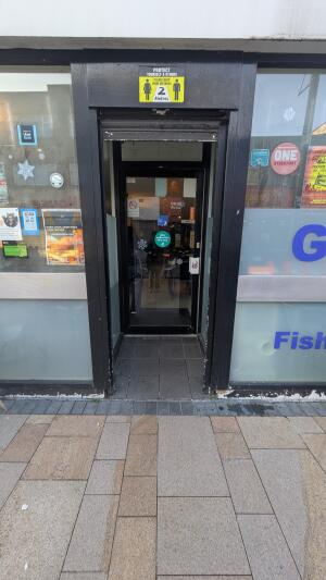 Black framed doorway followed by black metal-framed glass door. Pull from handle on left to open.