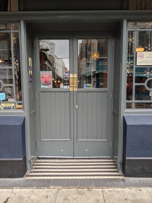 Glass and grey wood door with grey frame. Pull from metal handle in centre to open.
