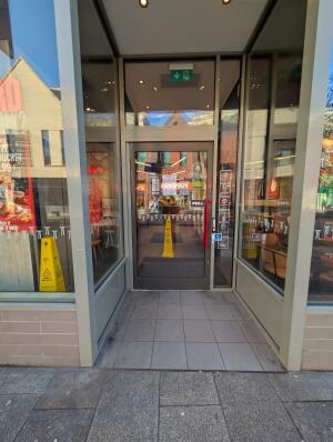 Light grey frame archway in front. Dark grey frame glass door at back. Red handle on right. Pull to open. Doorbell for assistance on right.