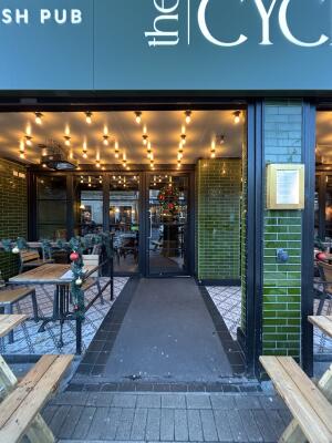 From sidewalk facing straight. Opening ahead between outdoor seating.