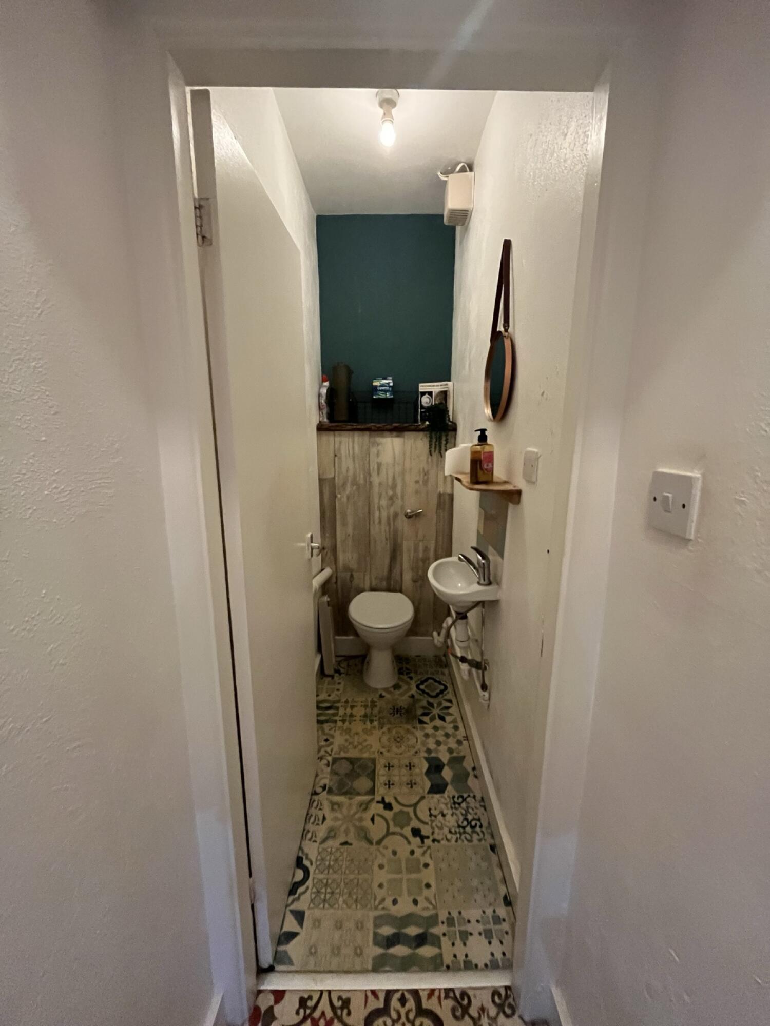 From end of corridor facing straight. White door with handle on right. Push to open. Sink on right wall. Toilet on back wall.