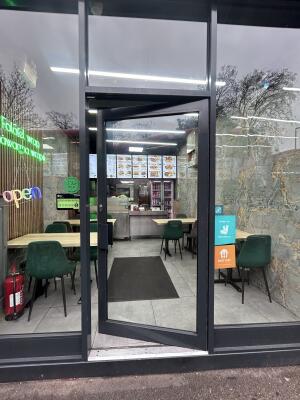 Glass door with grey metal frames ahead. Push handle on left to open.