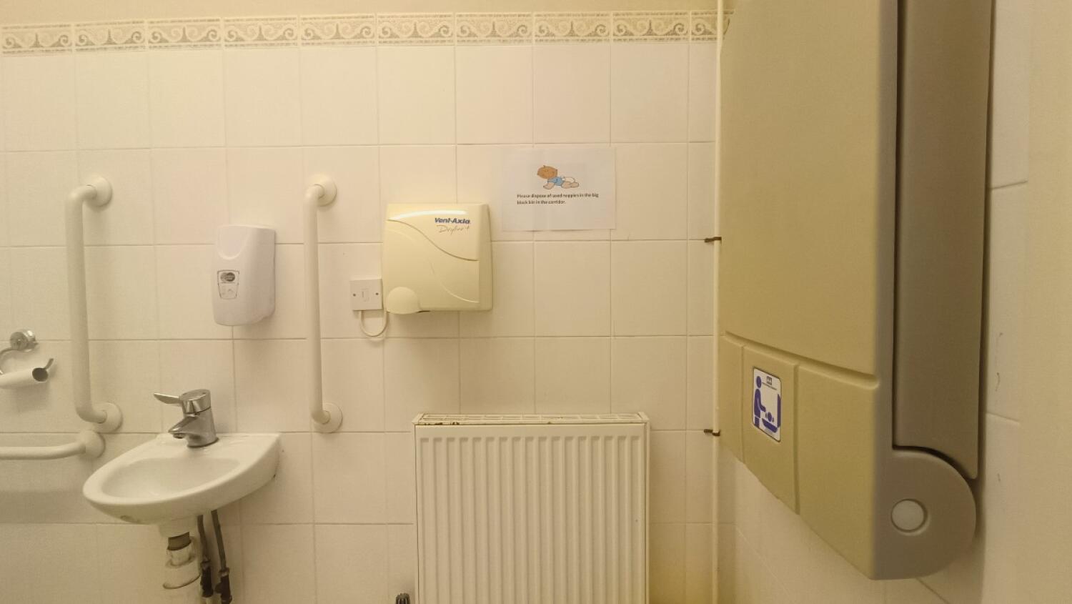 From door facing right. Sink on back left. Baby changing table along right.
