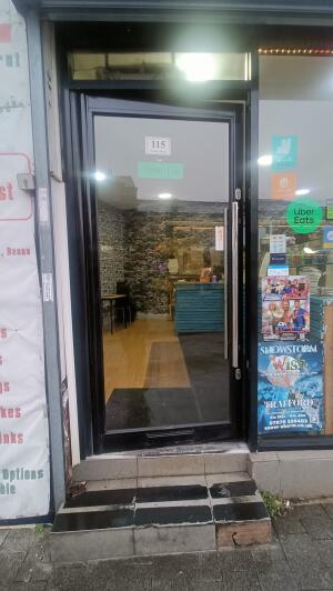 Black framed glass door to venue. Push handle on right to open.