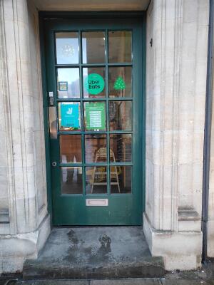 Green framed glass panel door ahead. Push silver bar on left to open.