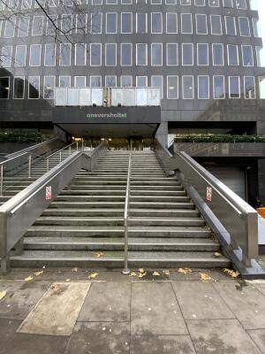 From Eversholt street facing building. Staircase ahead, leading up. Metal handrails along left, right and centre.