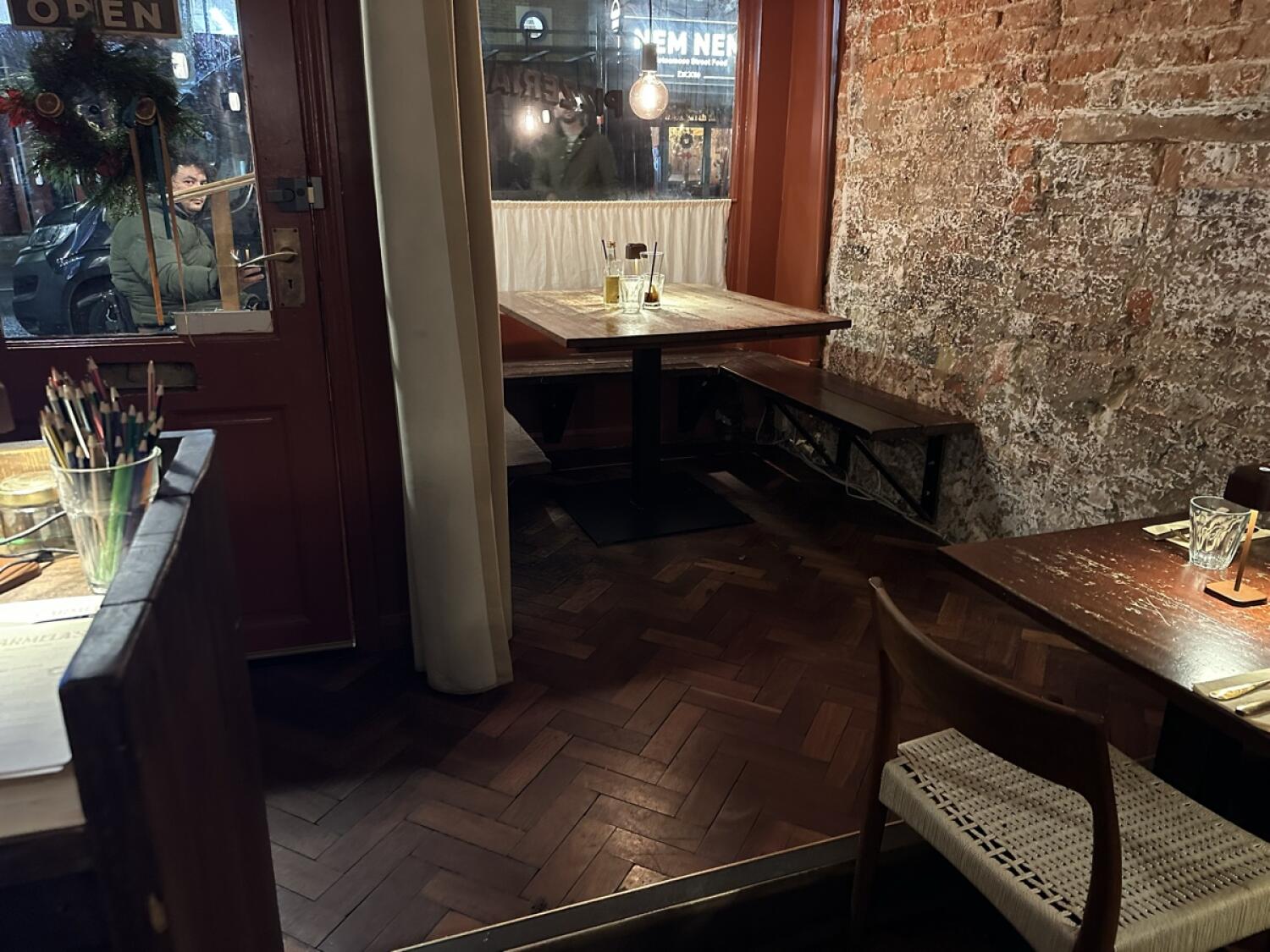 Half booth along back wall. Table with benches in centre. Table and chair in foreground right.