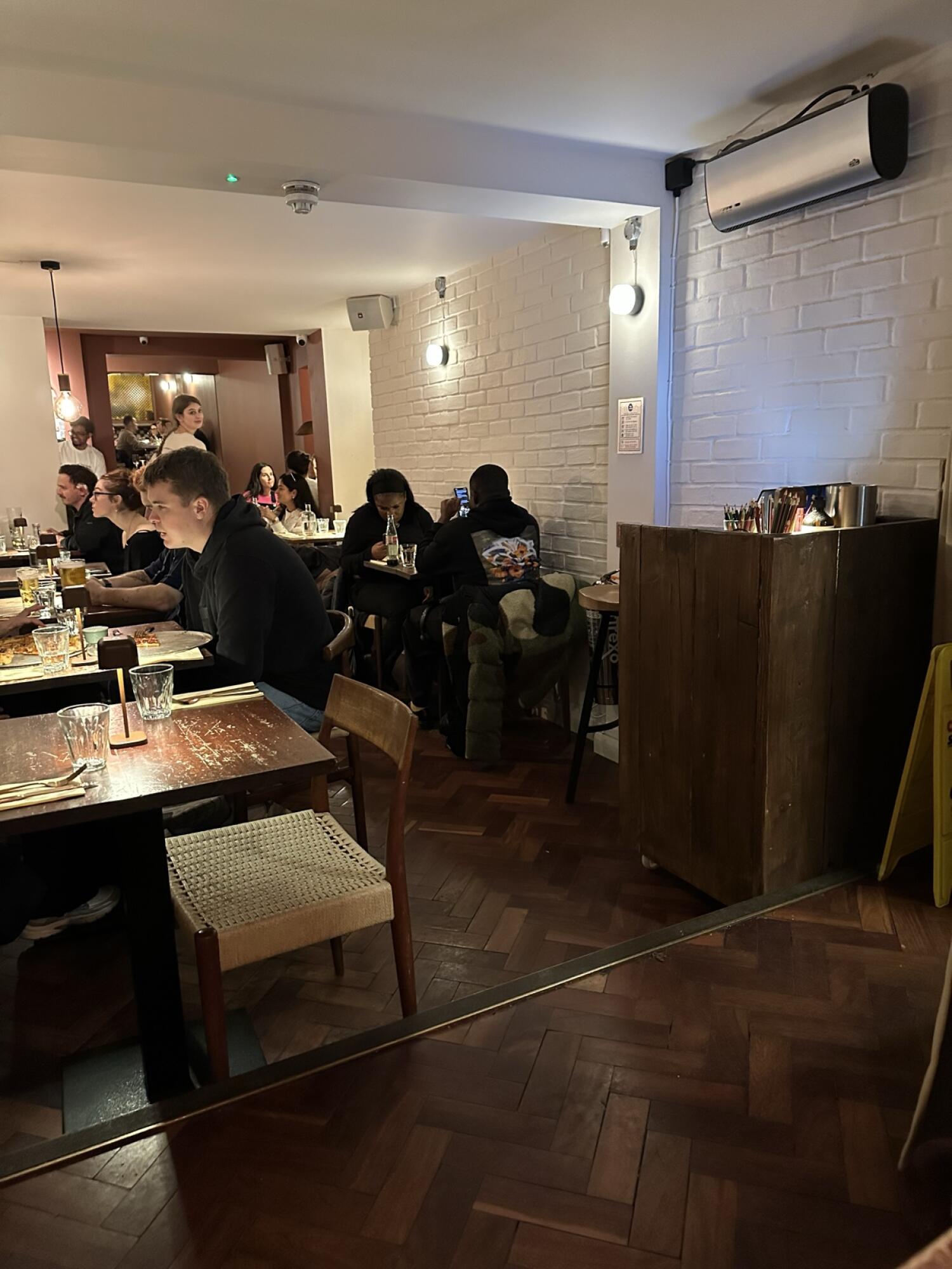 Tables and chairs along left. Path to back seating in centre. Wooden cabinet on right wall.