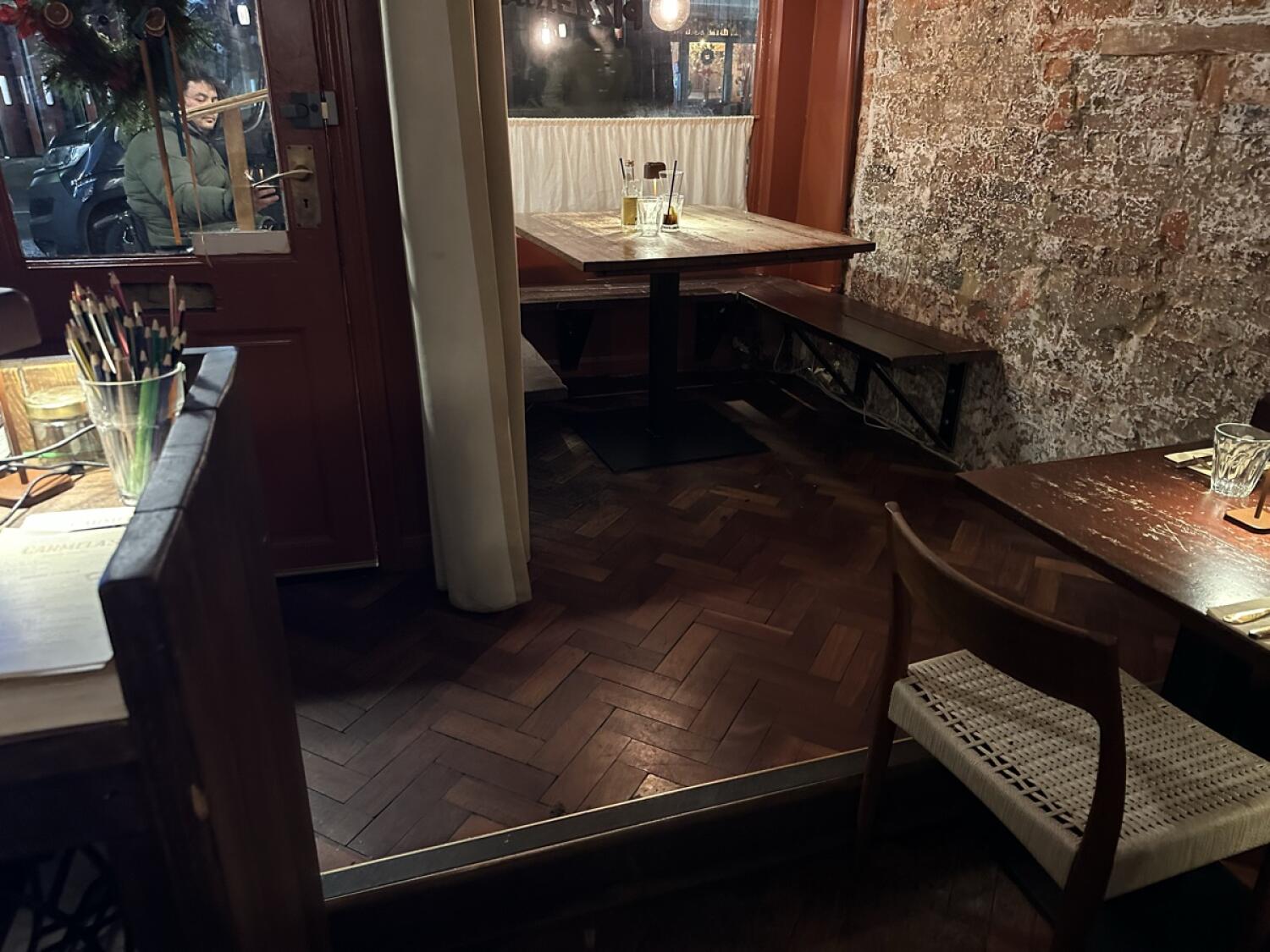 Half booth along back wall. Table with benches in centre. Table and chairs in foreground right.