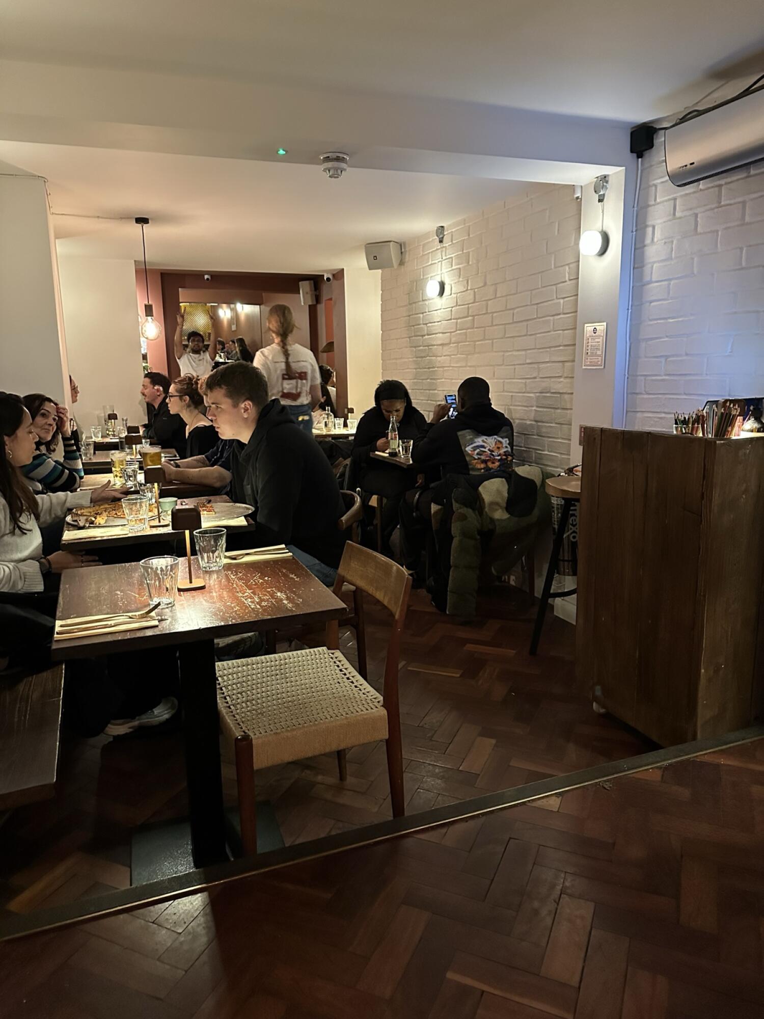 Tables and chairs along left. More tables in centre space. Wooden counter along right wall.