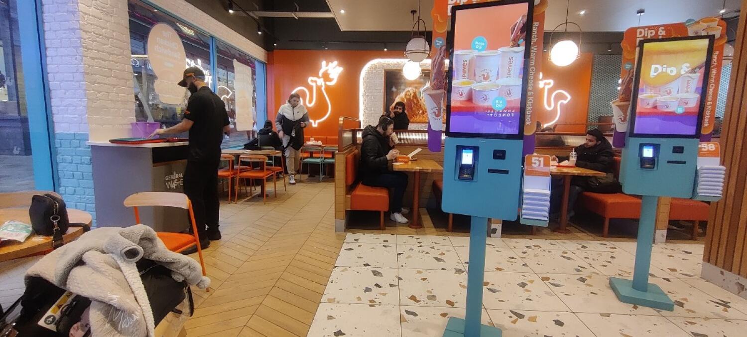 From entrance facing left. Tables and chairs along left . Kiosk on center and right. Booth along back right.