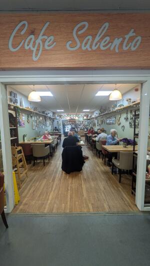 Open archway ahead. Tables and chairs along left and right. Display counter at back.