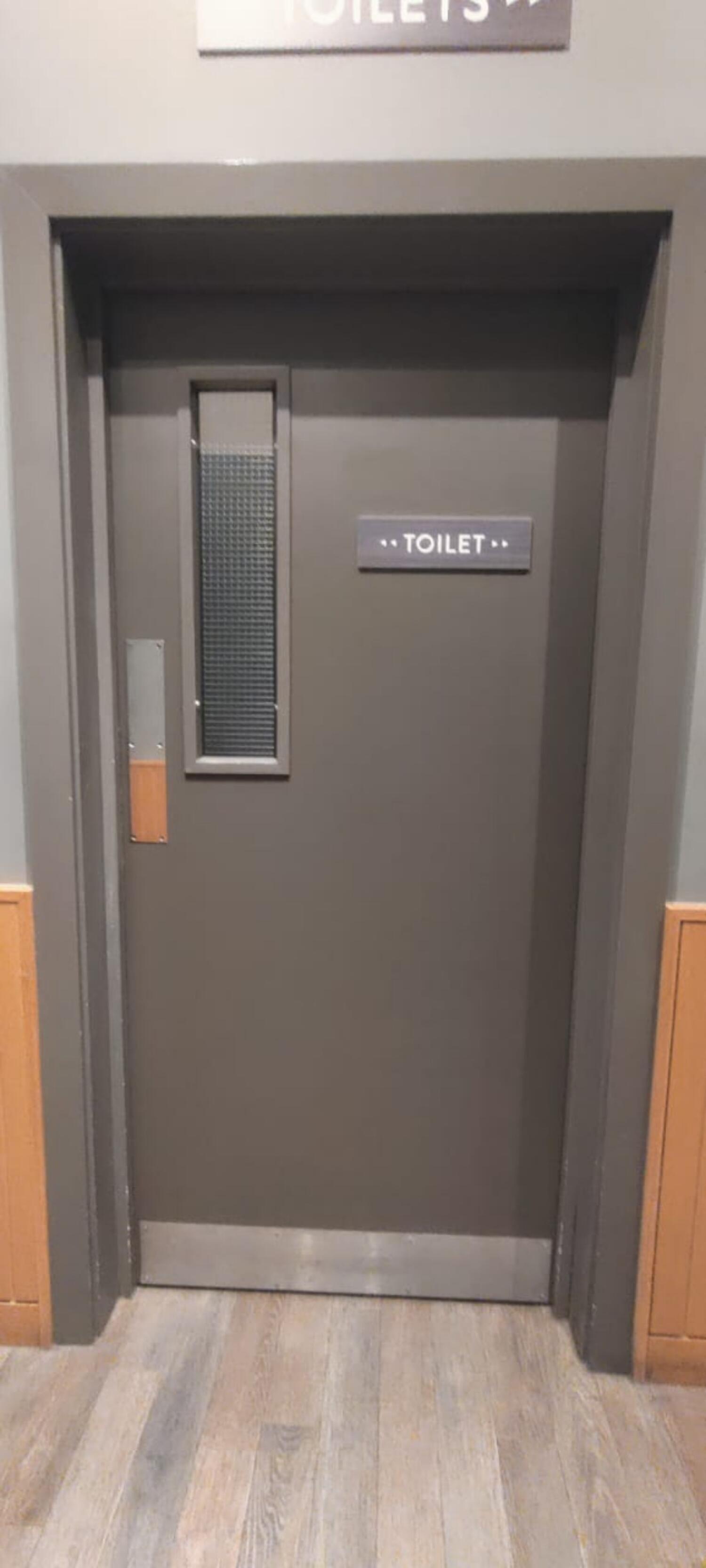 From center of path facing right. Grey wooden door ahead. Push bar at left.